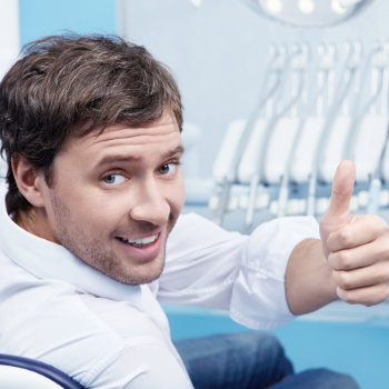a man with a healthy smile shows his thumbs up in the dentist chair
