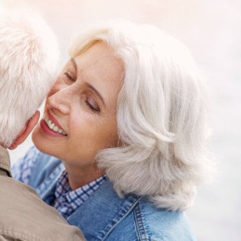 mature woman with a smile whispers something in her husbands ear