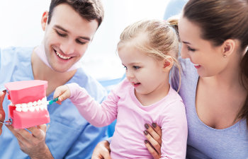 happy parents in the dental office showing the child a big plastic jaw